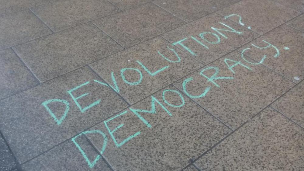 Message chalked on the pavement outside WYCA meeting, reading "How might devolution be more democratic?"