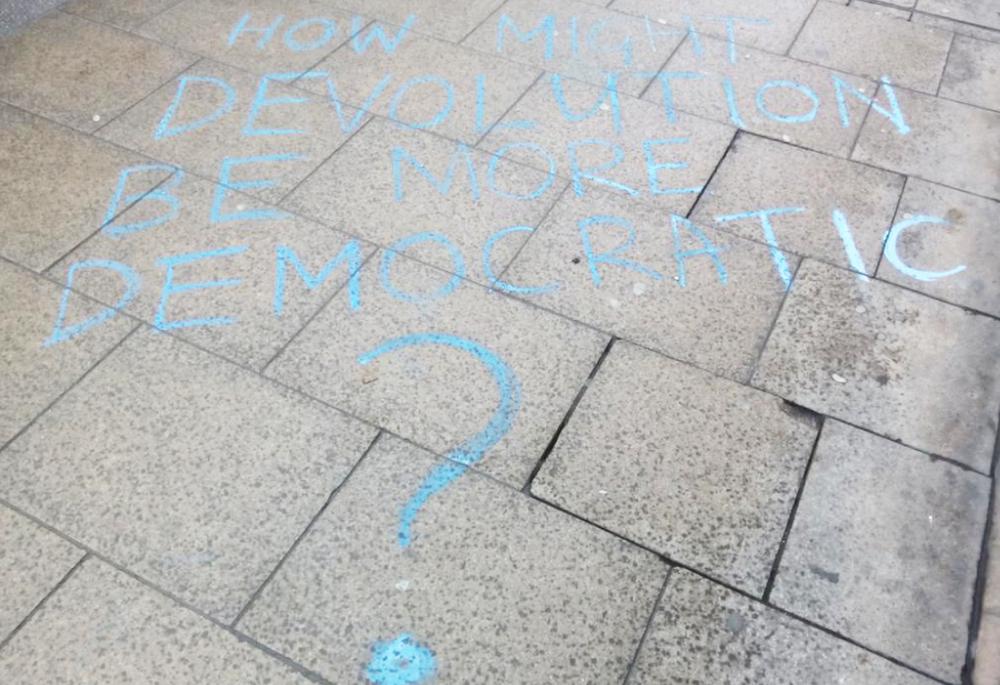 Message chalked on the pavement outside WYCA meeting, reading "How might devolution be more democratic?"