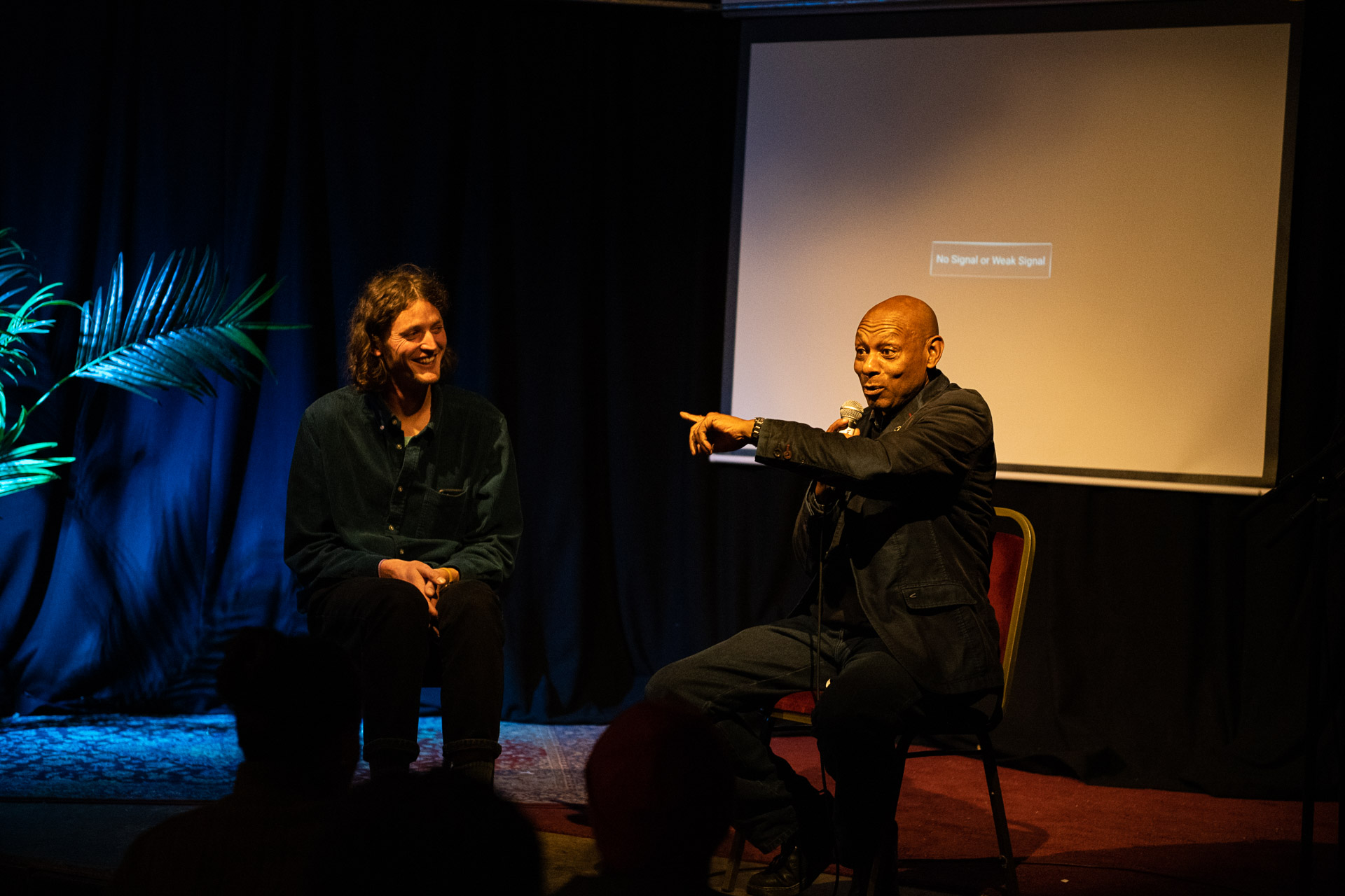 Claude Hendrickson and Neil Mckenna spotlighted in a small stage during a Q&A