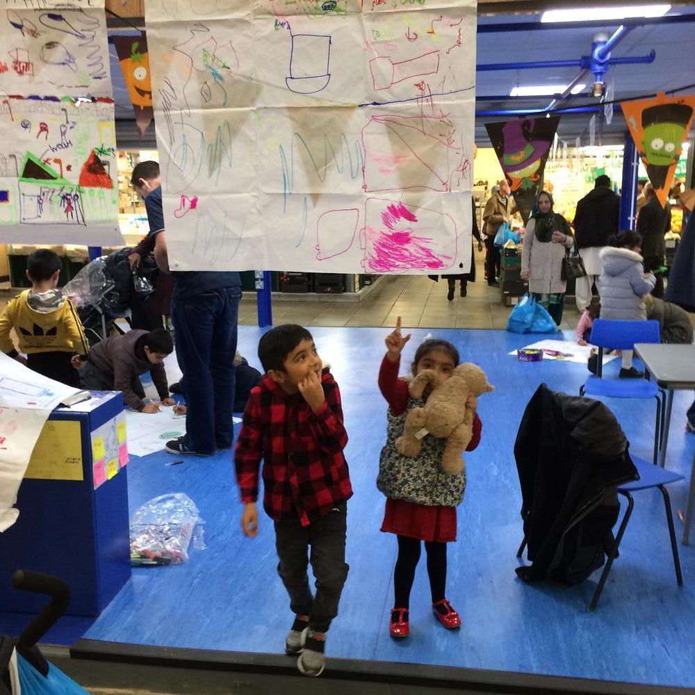 A small girl holding a teddybear points to her hand draw map in Bradford market