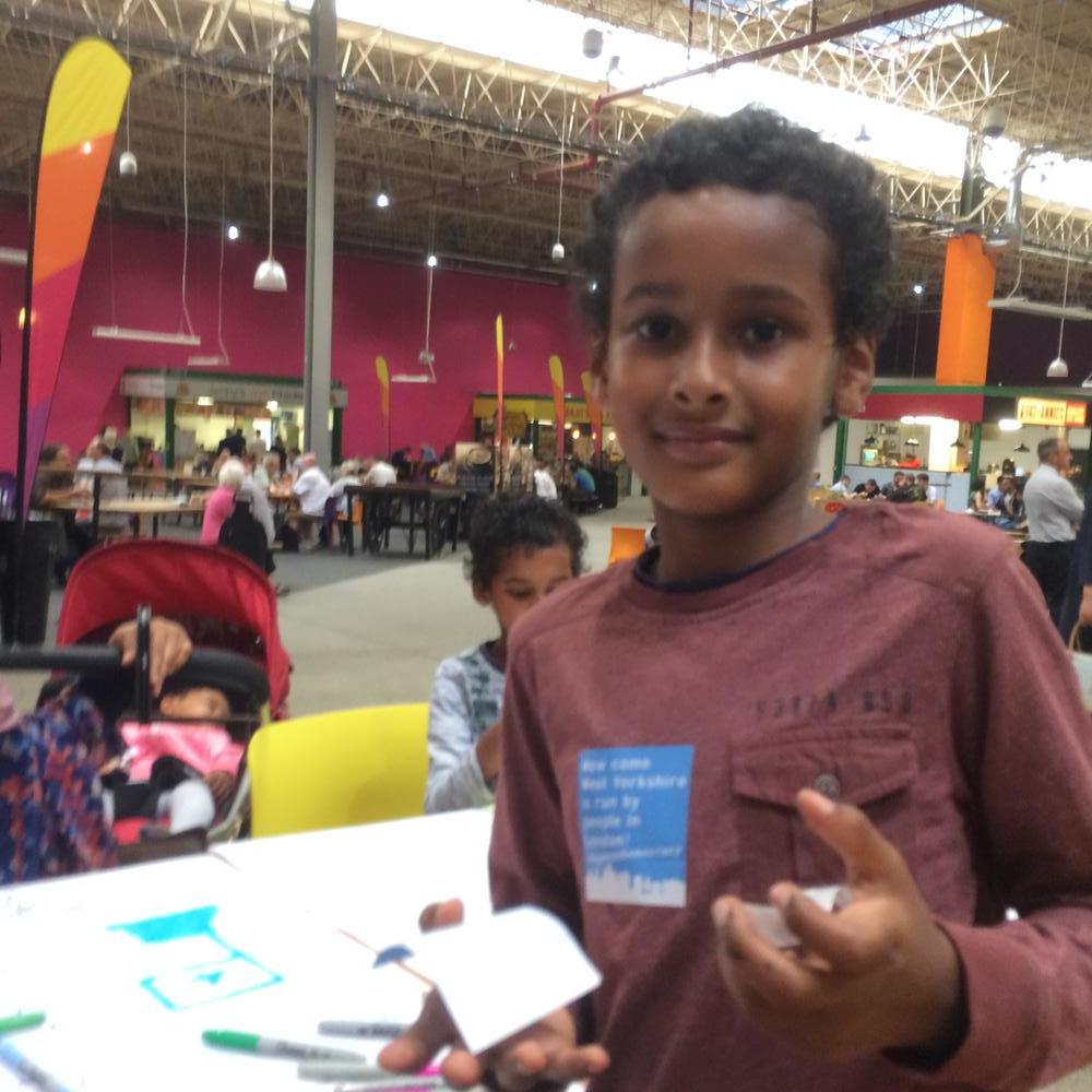 A boy wearing a Same Skies sticker in Leeds market