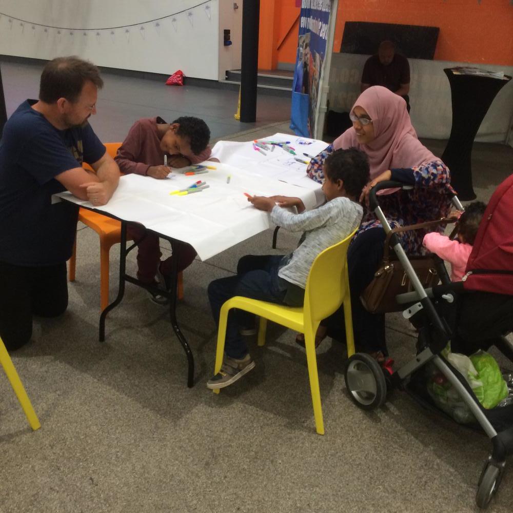 Ian Martin talking to a family drawing maps at table in Leeds market.